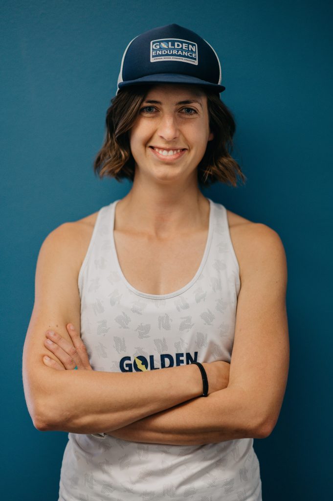 sammi smiling, she is wearing a white tank top with a Golden Endurance baseball hat